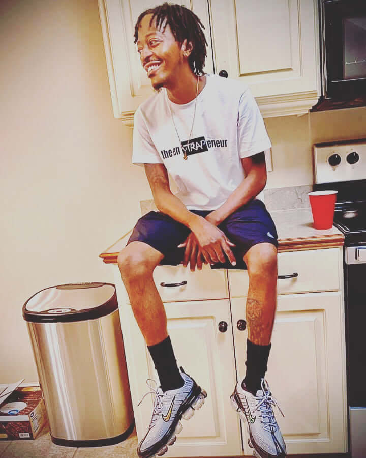 Man smiling in the enTRAPreneur T-Shirt, sitting in kitchen with a relaxed style.