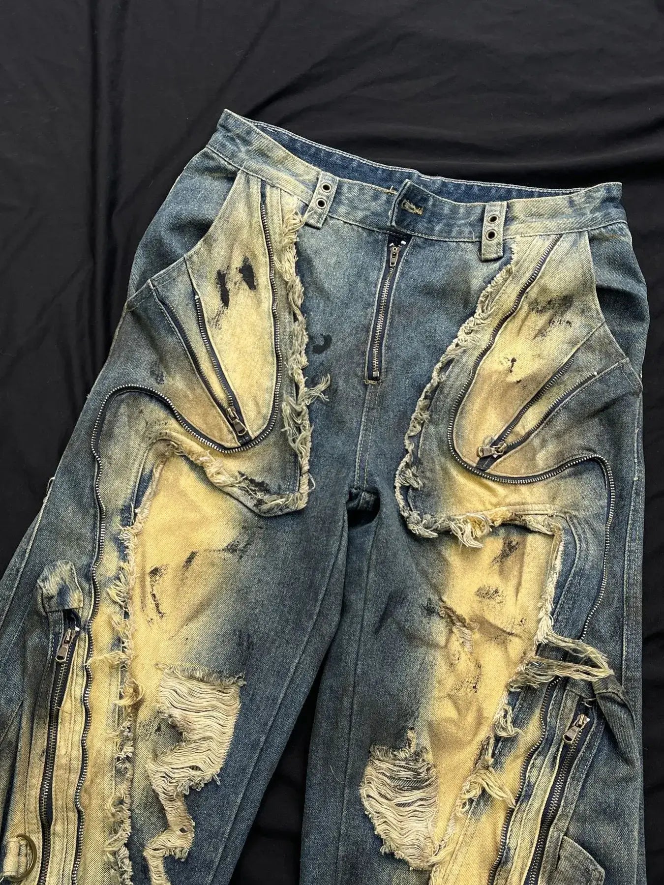 Distressed cargo jeans with artistic rips and pocket details on a dark backdrop.